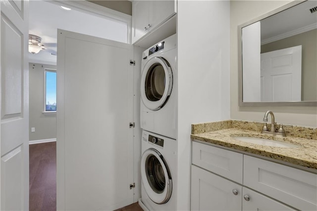 clothes washing area with sink, hardwood / wood-style flooring, ornamental molding, ceiling fan, and stacked washer / drying machine