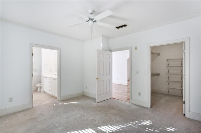 unfurnished bedroom with a spacious closet, a closet, light carpet, ceiling fan, and crown molding