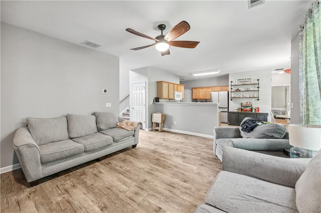living area featuring light wood finished floors, ceiling fan, stairway, and baseboards