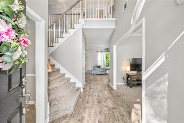 entrance foyer with stairs, a towering ceiling, baseboards, and wood finished floors