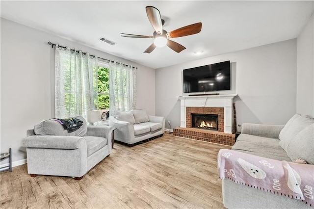 living room featuring ceiling fan, a fireplace, light wood-style flooring, and baseboards