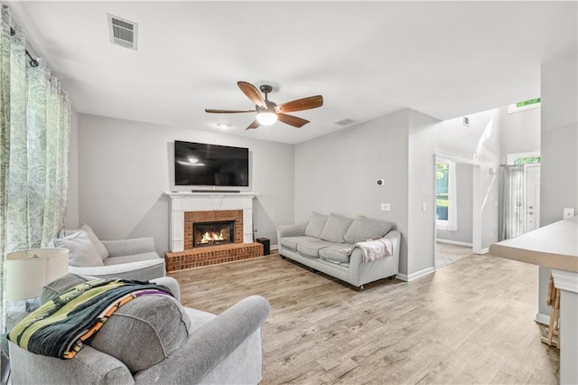 living area with a ceiling fan, light wood finished floors, a brick fireplace, and baseboards