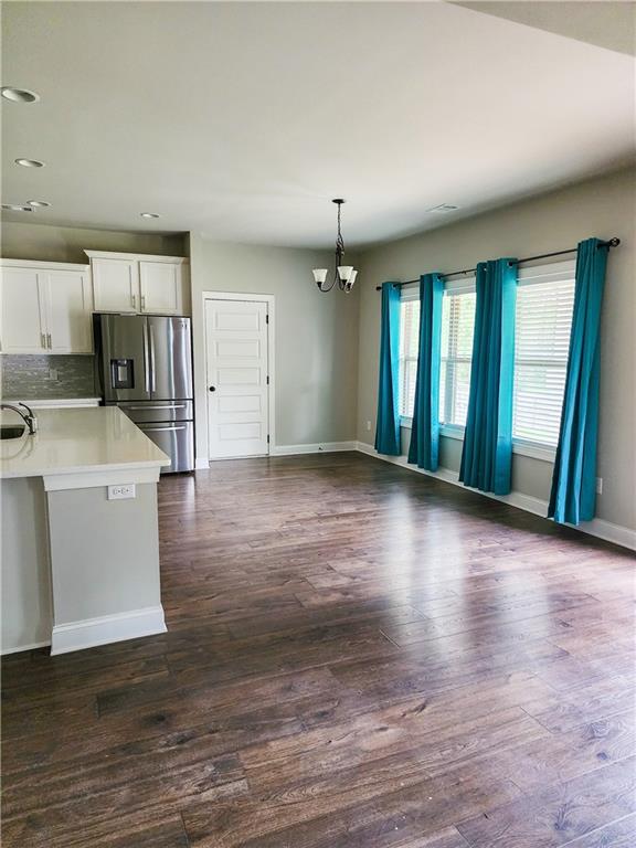 kitchen with stainless steel refrigerator with ice dispenser, hanging light fixtures, dark hardwood / wood-style floors, and white cabinetry