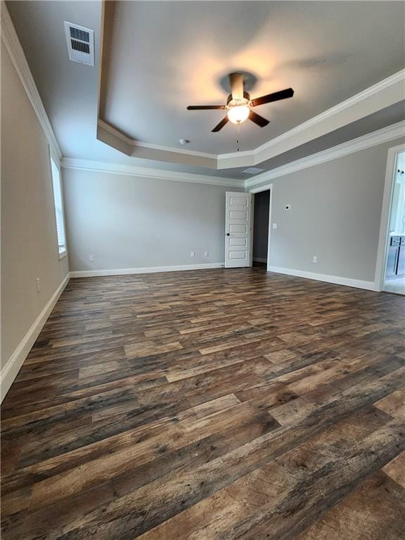 empty room featuring a tray ceiling, ceiling fan, dark wood-type flooring, and crown molding