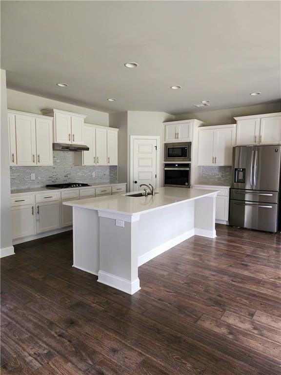 kitchen featuring a kitchen island with sink, tasteful backsplash, white cabinets, appliances with stainless steel finishes, and dark hardwood / wood-style flooring