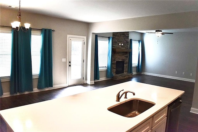 kitchen featuring sink, decorative light fixtures, dark wood-type flooring, a fireplace, and ceiling fan with notable chandelier