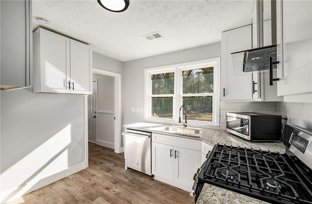 kitchen with light hardwood / wood-style floors, appliances with stainless steel finishes, white cabinets, sink, and light stone counters