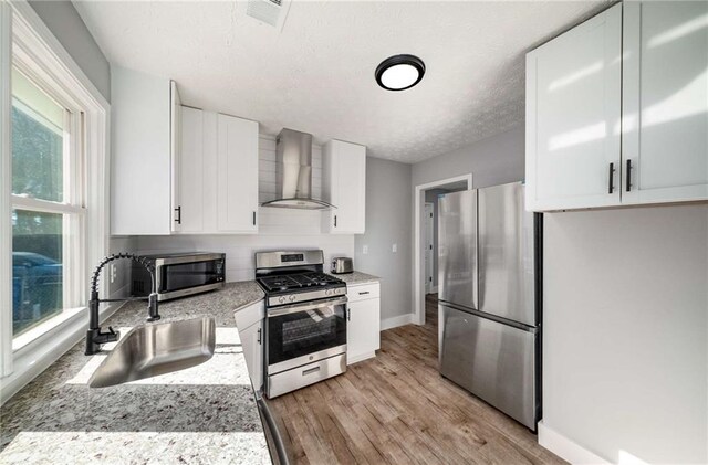 kitchen with wall chimney exhaust hood, white cabinets, a wealth of natural light, and appliances with stainless steel finishes