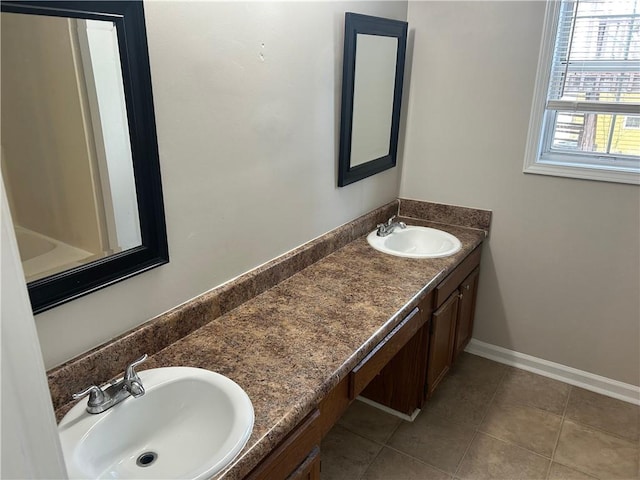 full bath featuring double vanity, tile patterned floors, a sink, and baseboards