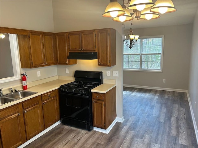 kitchen featuring brown cabinetry, gas stove, a sink, a chandelier, and under cabinet range hood