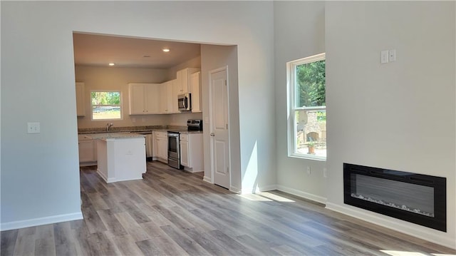 kitchen featuring stainless steel appliances, a center island, light stone counters, white cabinets, and light wood-type flooring