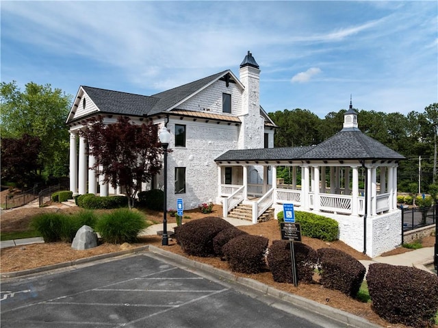 view of side of property with covered porch, uncovered parking, and a chimney