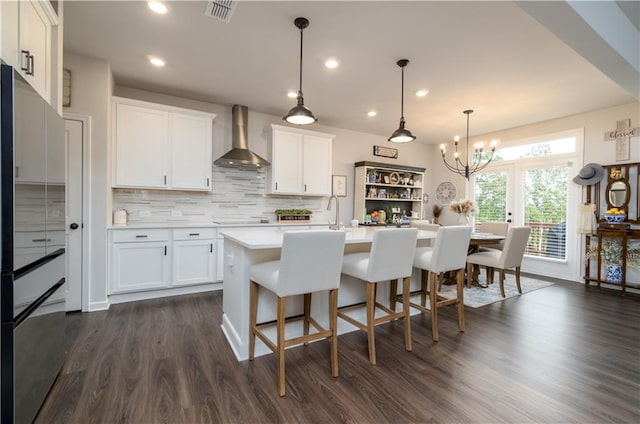 kitchen featuring wall chimney range hood, light countertops, a chandelier, white cabinetry, and tasteful backsplash