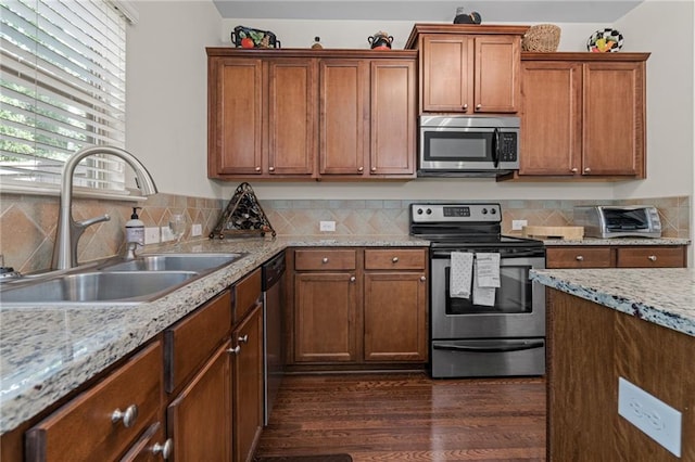 kitchen featuring appliances with stainless steel finishes, sink, backsplash, dark hardwood / wood-style flooring, and light stone counters