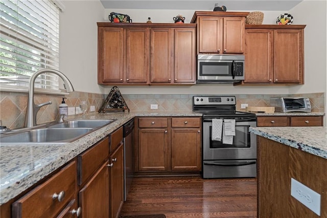 kitchen featuring appliances with stainless steel finishes, a sink, dark wood-style floors, decorative backsplash, and brown cabinetry