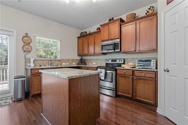 kitchen featuring a kitchen island, stainless steel appliances, sink, light stone countertops, and dark hardwood / wood-style flooring