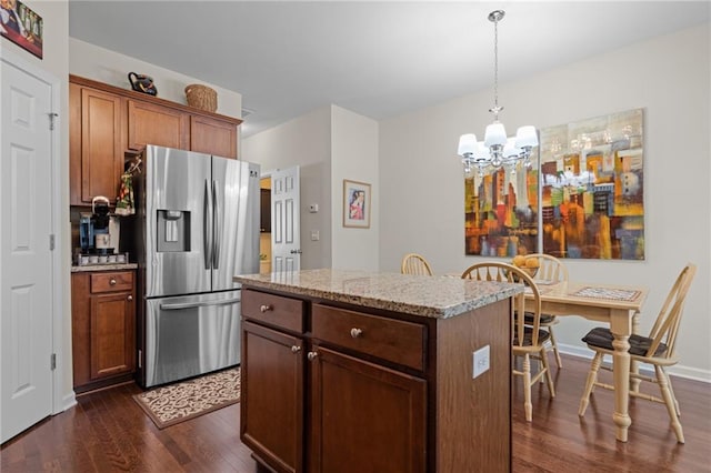 kitchen with light stone countertops, dark hardwood / wood-style floors, pendant lighting, stainless steel refrigerator with ice dispenser, and a center island