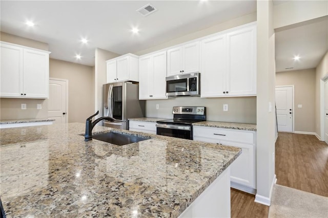 kitchen featuring light stone countertops, wood finished floors, a sink, appliances with stainless steel finishes, and white cabinetry