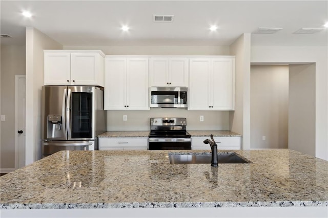 kitchen featuring light stone counters, visible vents, a sink, stainless steel appliances, and white cabinetry