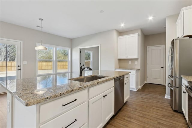 kitchen with light stone countertops, stainless steel appliances, wood finished floors, white cabinetry, and a sink