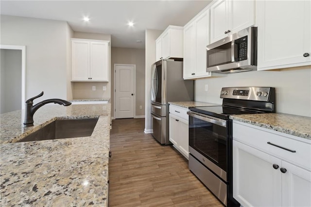 kitchen with a sink, wood finished floors, white cabinetry, appliances with stainless steel finishes, and light stone countertops