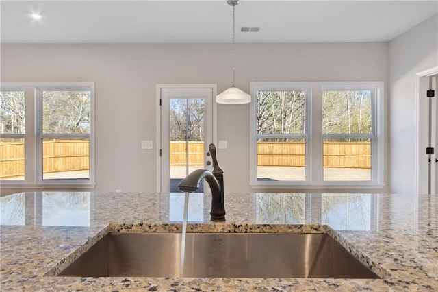 kitchen with light stone counters, visible vents, pendant lighting, and a sink