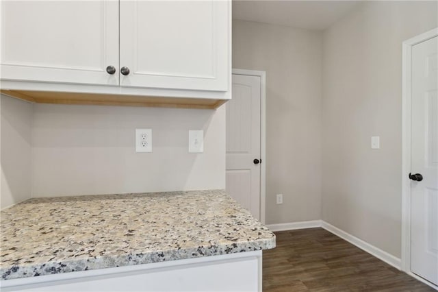 interior space featuring white cabinetry, dark wood-type flooring, light stone counters, and baseboards