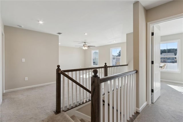 hall with visible vents, an upstairs landing, carpet, and a healthy amount of sunlight