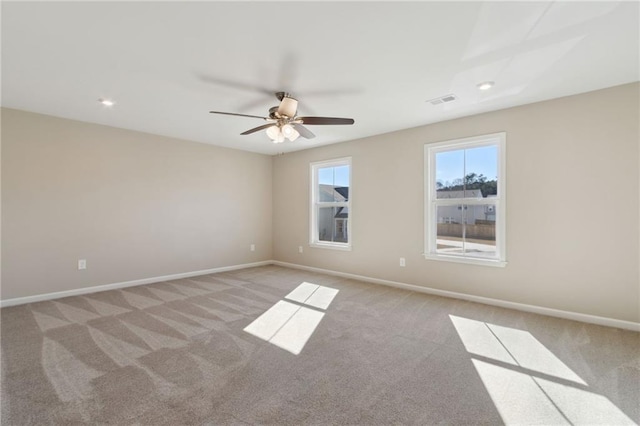 empty room featuring visible vents, light colored carpet, a ceiling fan, and baseboards