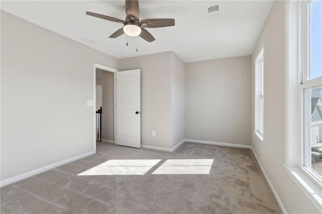 carpeted empty room with visible vents, ceiling fan, and baseboards