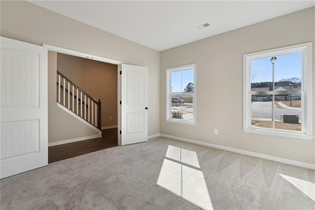 carpeted empty room featuring stairway, baseboards, and visible vents