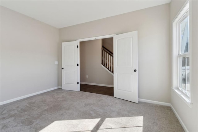 carpeted spare room with stairway, baseboards, and a healthy amount of sunlight