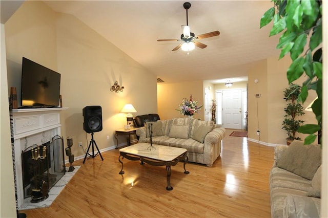 living room with ceiling fan, vaulted ceiling, a fireplace, and light hardwood / wood-style floors