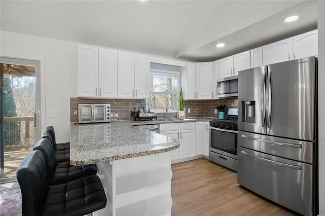 kitchen featuring white cabinets, appliances with stainless steel finishes, backsplash, vaulted ceiling, and light stone counters