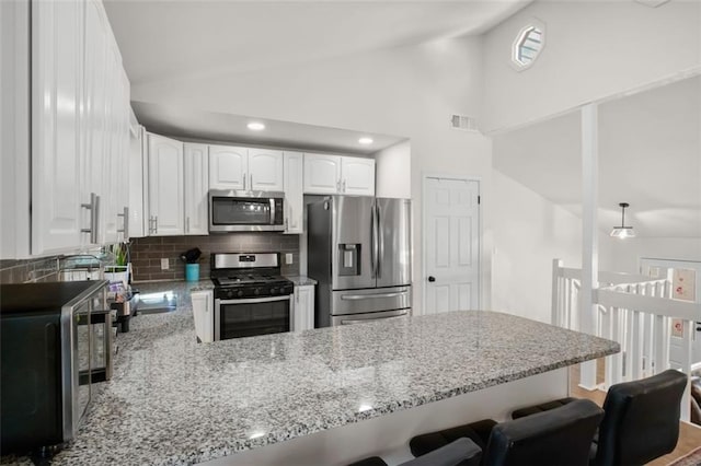 kitchen with backsplash, kitchen peninsula, white cabinetry, light stone countertops, and appliances with stainless steel finishes