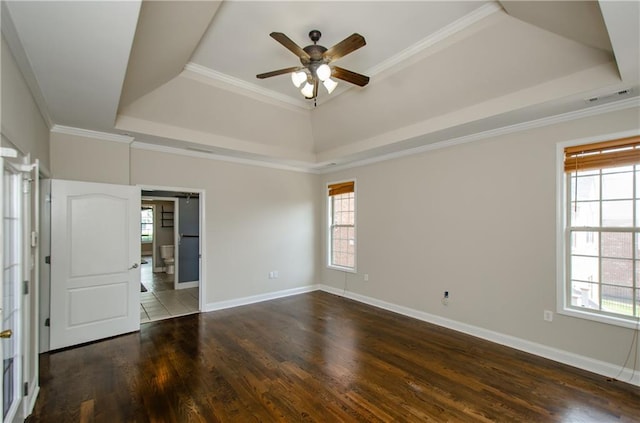 empty room featuring a tray ceiling, ceiling fan, wood finished floors, baseboards, and ornamental molding