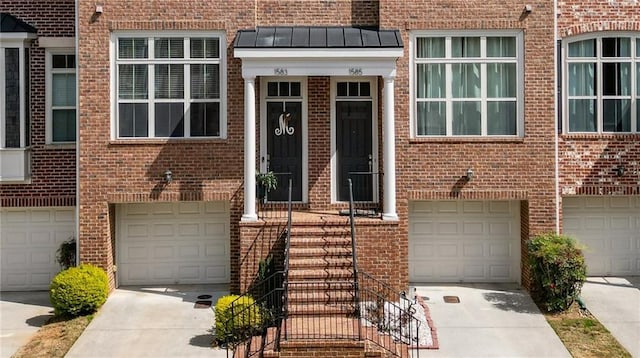 view of exterior entry featuring metal roof, brick siding, an attached garage, and a standing seam roof