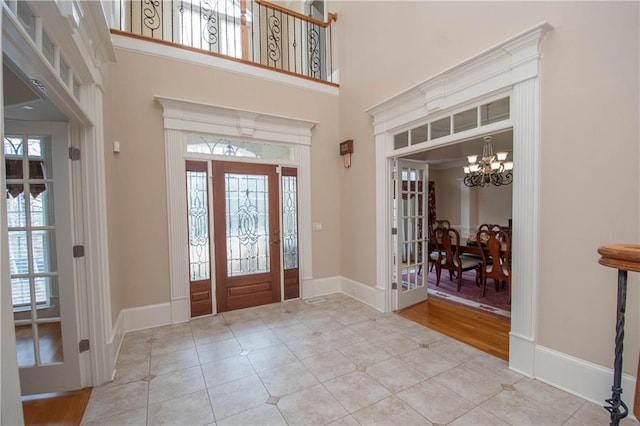 tiled entrance foyer with a notable chandelier, a high ceiling, and baseboards