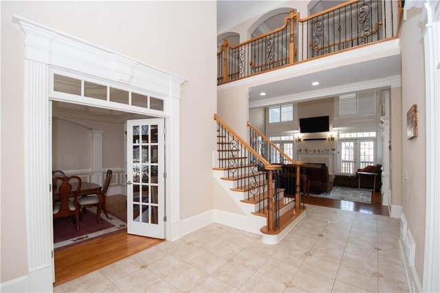 tiled entrance foyer with a fireplace, stairs, crown molding, and a towering ceiling