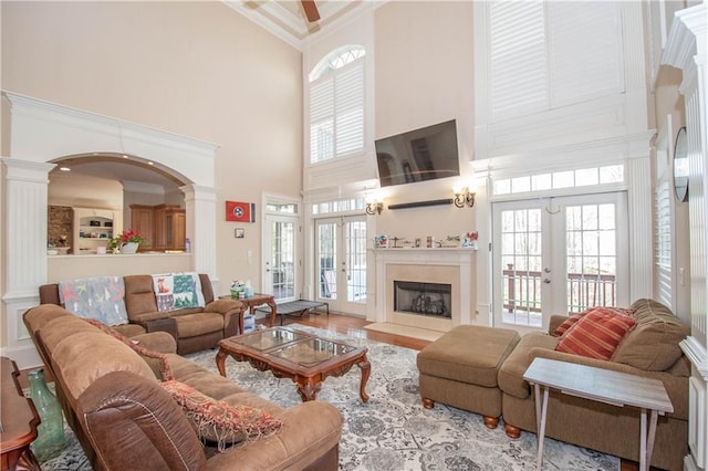 living area featuring a fireplace, decorative columns, french doors, and a towering ceiling