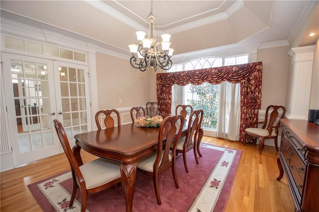 dining area featuring light wood finished floors, crown molding, french doors, a notable chandelier, and a raised ceiling