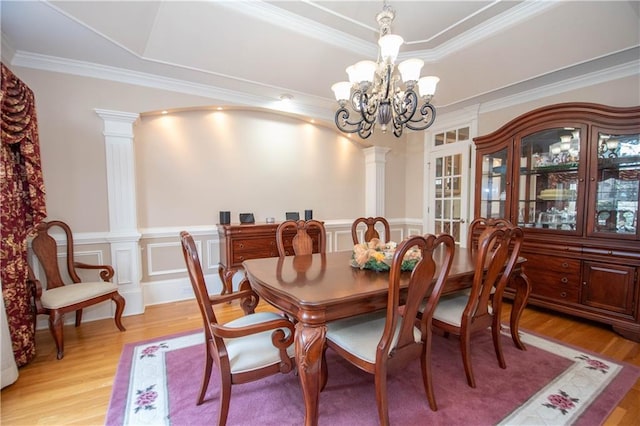 dining space featuring light wood finished floors, a chandelier, a tray ceiling, and decorative columns