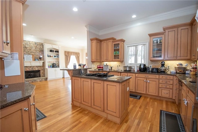 kitchen featuring light wood-style flooring, open floor plan, stainless steel gas stovetop, crown molding, and glass insert cabinets