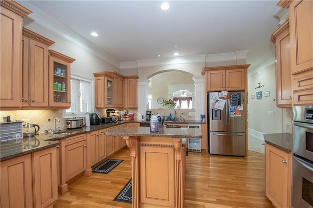 kitchen featuring ornate columns, light wood finished floors, arched walkways, glass insert cabinets, and appliances with stainless steel finishes