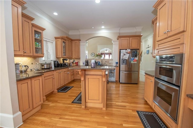 kitchen with a center island, appliances with stainless steel finishes, light wood-style floors, arched walkways, and ornate columns