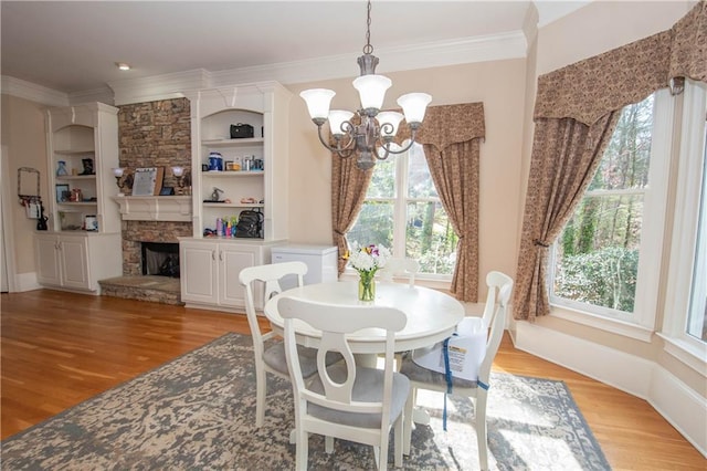 dining room featuring built in features, a notable chandelier, ornamental molding, and light wood finished floors