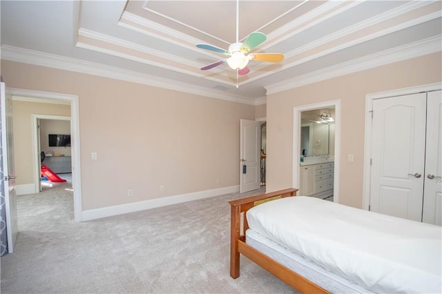 carpeted bedroom featuring crown molding, baseboards, a tray ceiling, a closet, and ensuite bath