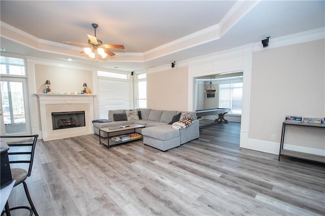 living room featuring crown molding, baseboards, a tray ceiling, wood finished floors, and a ceiling fan