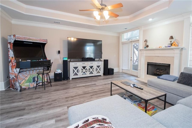 living room with a high end fireplace, ceiling fan, ornamental molding, wood finished floors, and a raised ceiling