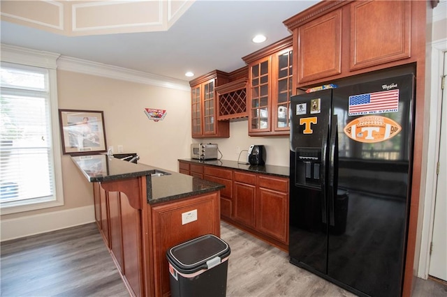 kitchen featuring brown cabinetry, dark stone counters, crown molding, light wood-type flooring, and black fridge